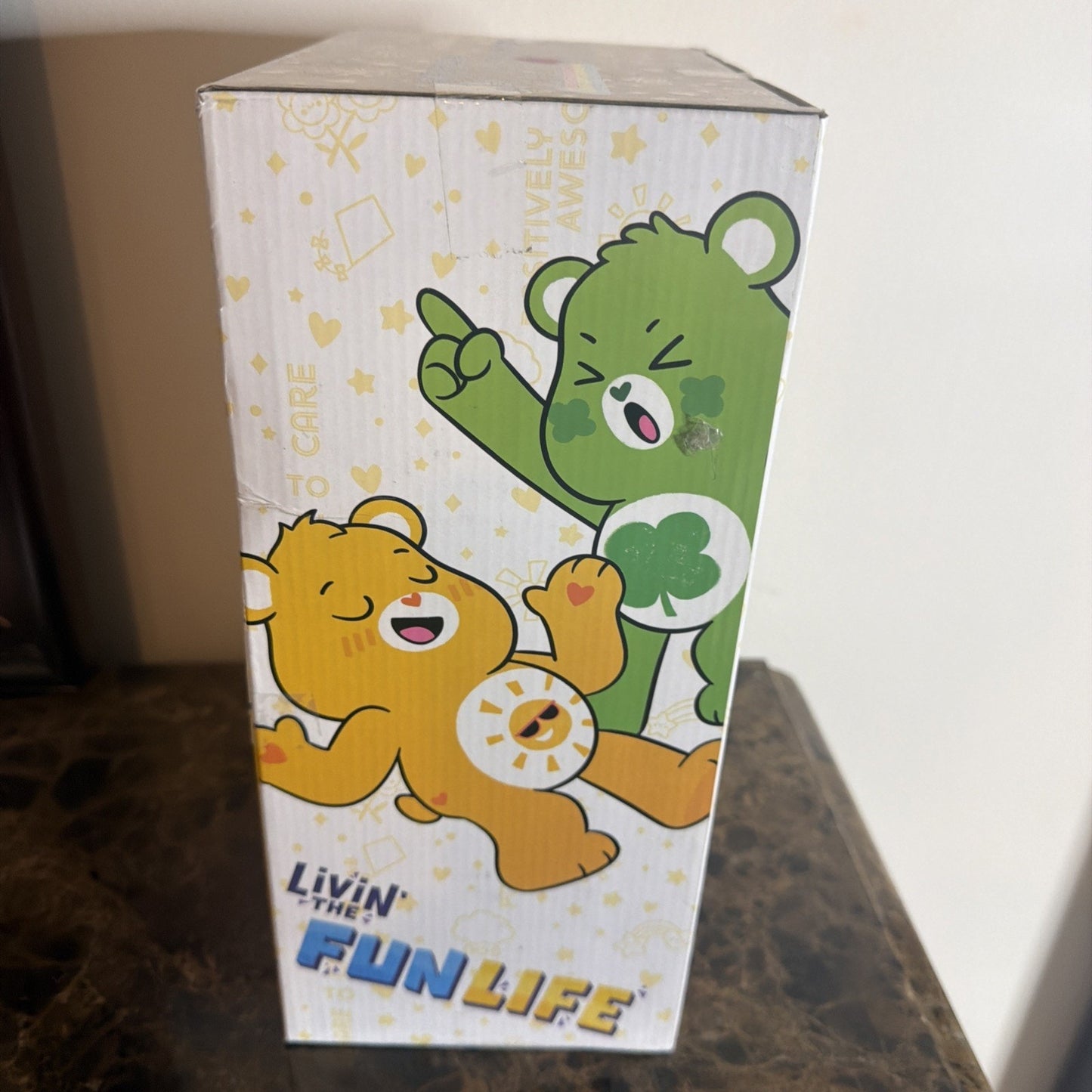 Side view of a decorative box showing two playful cartoon bears, one green with a clover emblem and one orange with a sun emblem, accompanied by the text "Livin’ the Fun Life" in colorful letters.