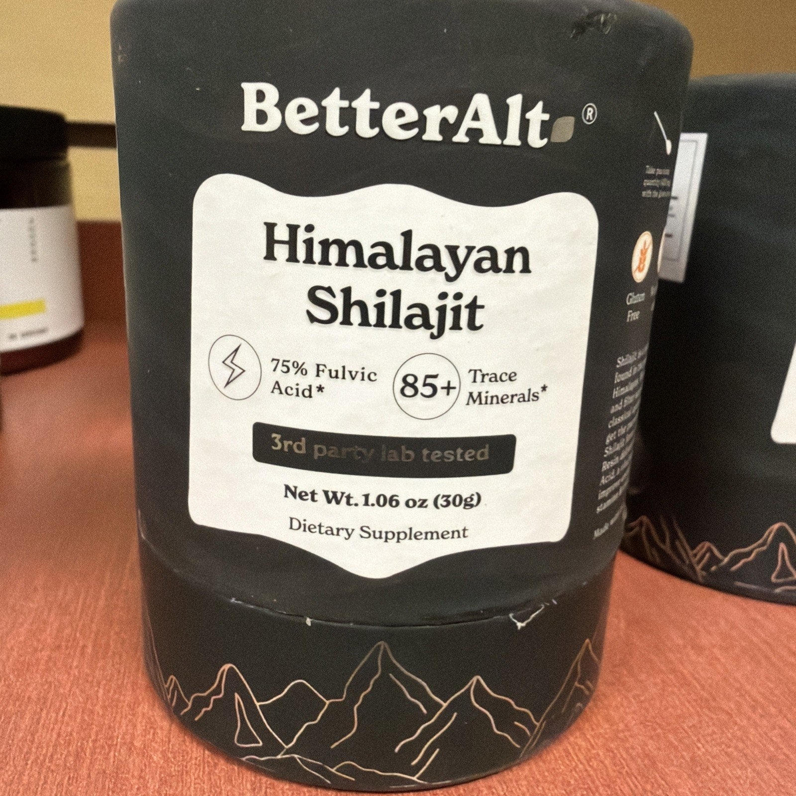 Black container of BetterAlt Himalayan Shilajit dietary supplement featuring 75% fulvic acid, over 85 trace minerals, 3rd party lab tested, with net weight of 1.06 oz (30g) and mountain design on the bottom.