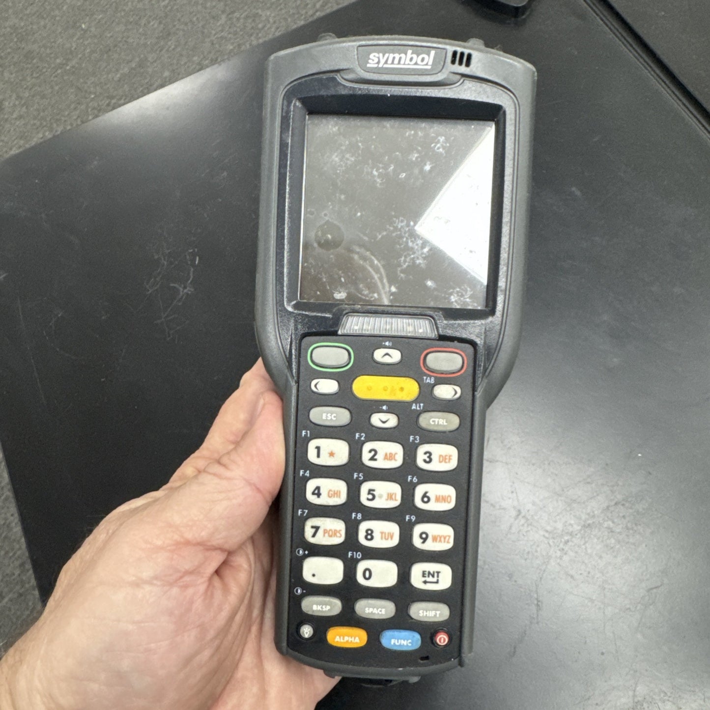 Handheld Motorola Symbol MC3090 mobile barcode scanner with screen and keypad held in hand on black surface