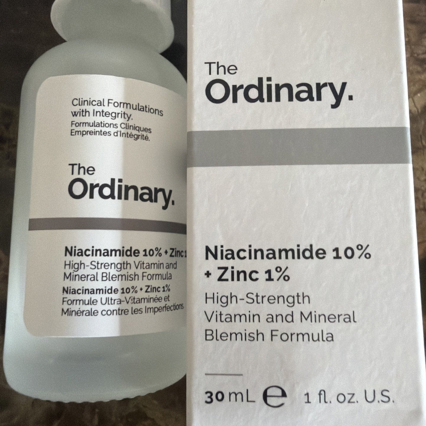 Frosted glass dropper bottle and white box of The Ordinary Niacinamide 10% + Zinc 1% serum featuring black text describing the high-strength vitamin and mineral blemish formula.