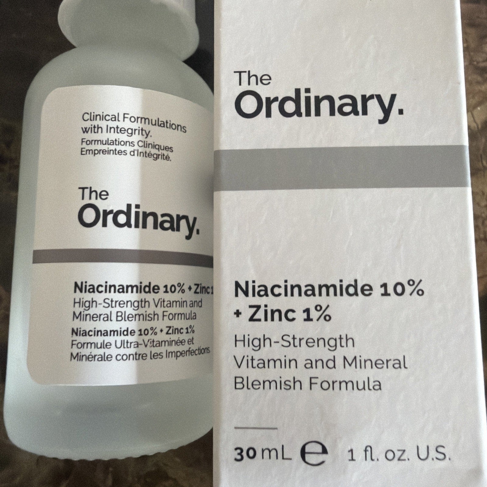 Frosted glass dropper bottle and white box of The Ordinary Niacinamide 10% + Zinc 1% serum featuring black text describing the high-strength vitamin and mineral blemish formula.