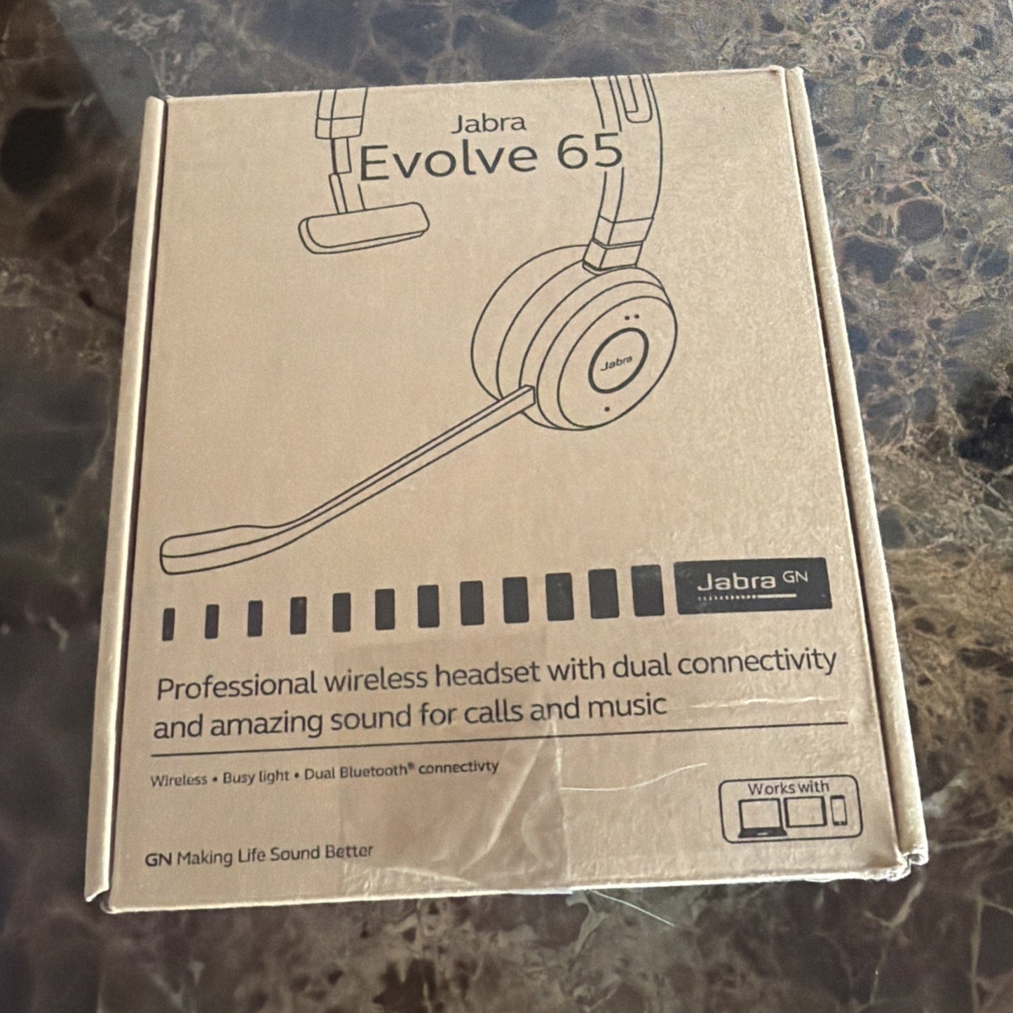 Brown cardboard box packaging for a Jabra Evolve 65 professional wireless headset, featuring a line drawing of the headset with boom microphone and text highlighting dual Bluetooth connectivity and sound quality for calls and music.
