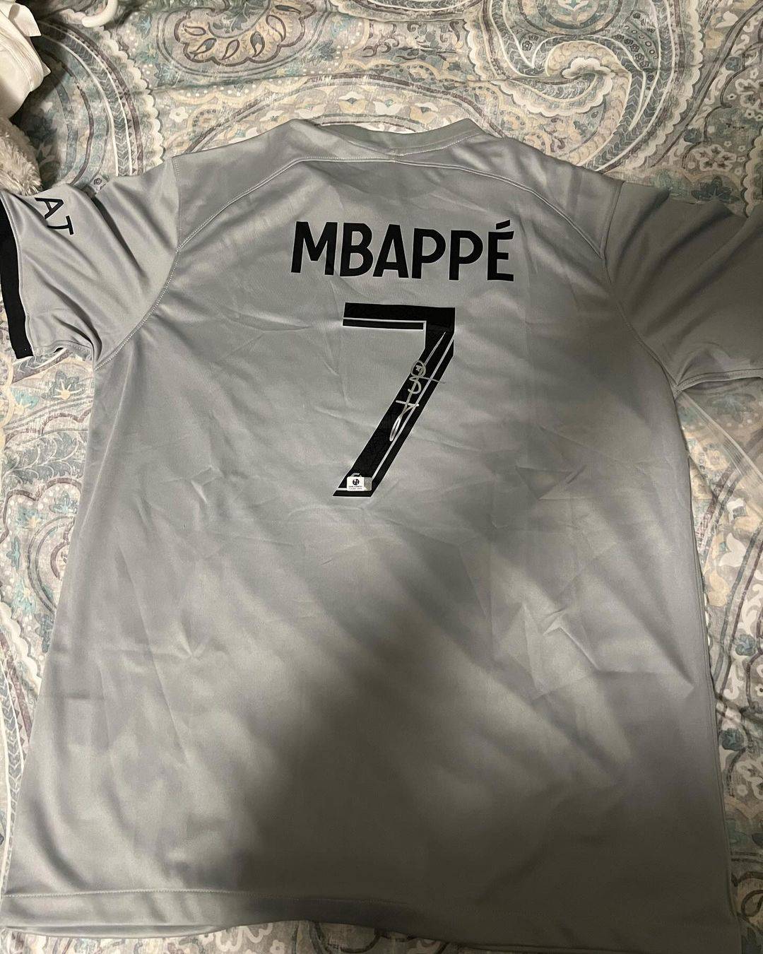 Back of autographed Kylian Mbappe PSG jersey with number 7 on light gray fabric background