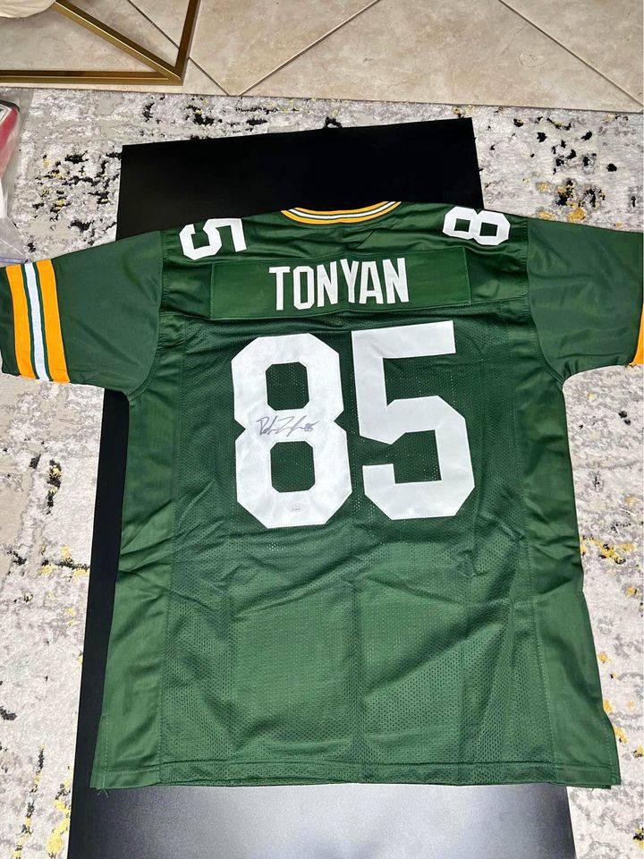 Green Robert Tonyan football jersey number 85 with autograph on back, laid flat on surface.