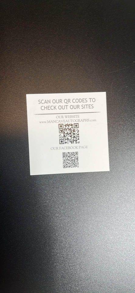 QR codes on a white card with website and Facebook page details for Mancave Autographs on a dark surface